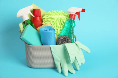 Açık mavi arka planda sepette farklı temizlik ürünleri