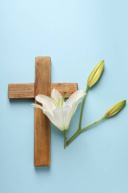 Ahşap haç ve açık mavi arka planda zambak çiçekleri, üst manzara. Paskalya özellikleri