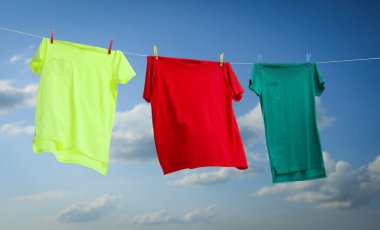 Mavi gökyüzüne karşı çamaşır ipinde kurutulan renkli tişörtler, pankart tasarımı