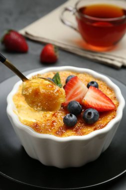 Gri masadaki kaseden alınan meyvelerle nefis bir creme brulee, yakın plan.