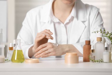 Dermatolog, beyaz masada el kremi sürüyor, yakın plan. Kozmetik ürünü test ediliyor