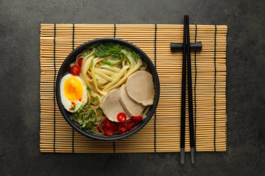 Kasede et ve gri desenli masada yemek çubukları olan lezzetli ramen, üst manzara. Erişte çorbası.