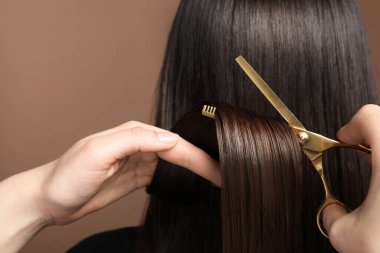 Kuaför açık kahverengi arka planda makasla müşterinin saçını kesiyor.