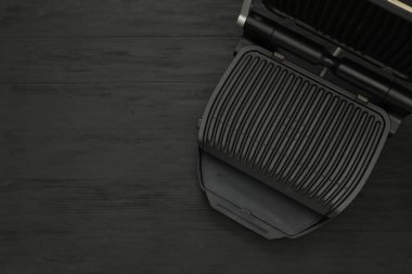 Siyah ahşap masada elektrikli ızgara, üst manzara. Mesaj için yer var. Yemek pişirme aygıtı
