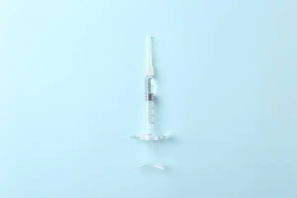 Cosmetology. Medical syringe on light blue background, top view