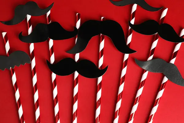 Fake paper mustaches with party props on red background, flat lay