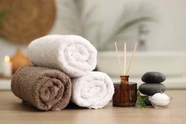 Spa kompozisyonu. Yuvarlak havlular, aroma yayıcı, masaj taşları ve yanan mumlar kapalı masa üzerinde.