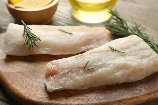 Fresh raw cod fillets with rosemary on wooden table, closeup