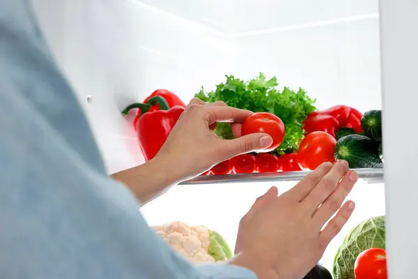 Young woman taking tomato out of refrigerator, closeup