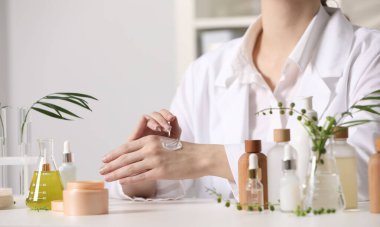 Dermatolog, beyaz masada el kremi sürüyor, yakın plan. Kozmetik ürünü test ediliyor