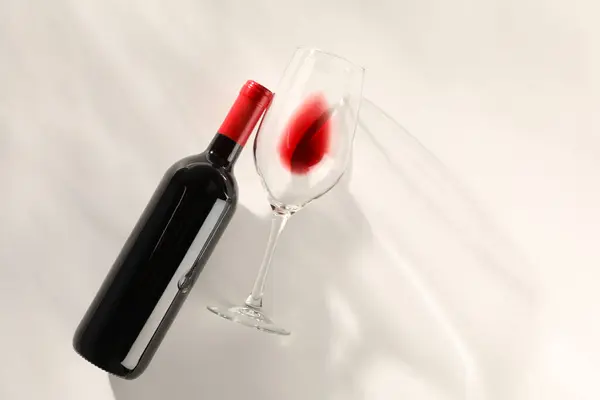Bottle of expensive red wine and wineglass on light background, top view. Space for text