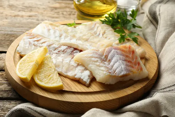 Fresh raw cod fillets, parsley and lemon on wooden table, closeup