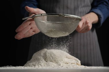 Ekmek yapıyorum. Masada hamuru elemekte olan kadın, yakın plan.