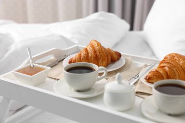 Yatakta servis edilen lezzetli kahvaltı. Taze kruvasanlar, tepside kahve ve bal, yakın plan.