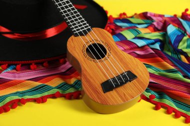 Siyah Flamenko şapka, panço ve ukulele sarı masada, yakın plan.