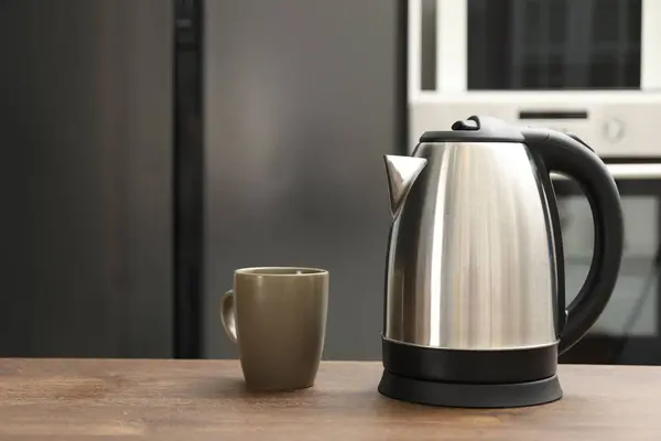 Modern electric kettle and cup on table in kitchen. Space for text