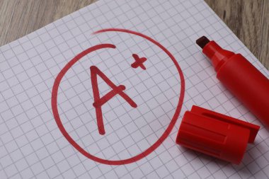 Okul derecesi. Kırmızı harf A, üzerinde artı işareti olan defter kağıdı ve işaret tablosu, yakın plan