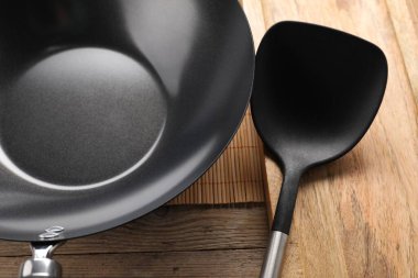 Black metal wok ve spatula ahşap masada, yakın plan.