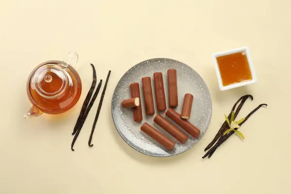 Glazed curd cheese bars, vanilla pods and tea on beige background, flat lay