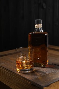 Buzlu viski, cam küplü ve siyah arka planda tahta sandıkta şişe.