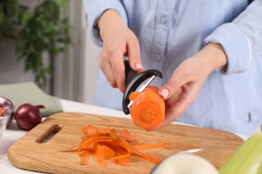 İçerideki masada taze havuç soyan kadın, yakın plan.