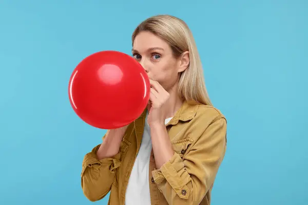 stock image Woman blowing up balloon on light blue background