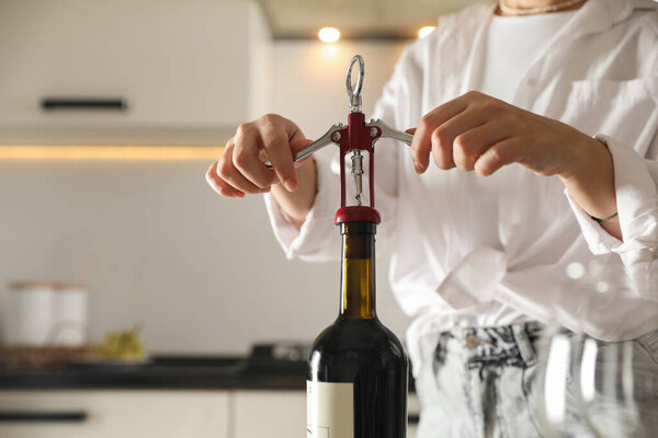 Woman opening wine bottle with corkscrew indoors, closeup. Space for text