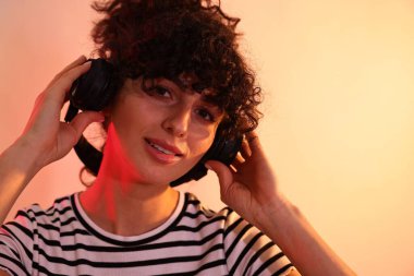 Güzel, genç bir kadın kulaklıkla müzik dinliyor. Renkli arka planda, neon ışıklarla, yakın plan. Metin için boşluk