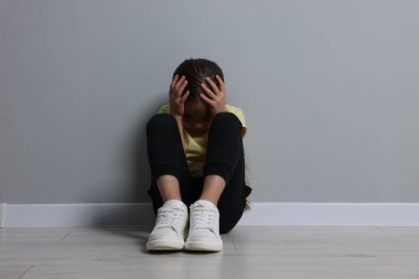 Çocuk istismarı. Üzgün kız gri duvarın yanında oturuyor.