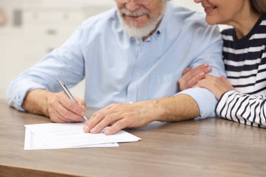 Ahşap masada son dilek ve vasiyetnameyi imzalayan mutlu çift, yakın plan.