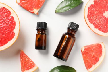 Şişelerde greyfurt yağı, yapraklar ve beyaz masa üzerinde meyve kesimi, düz uzanış