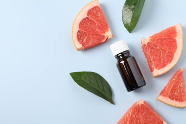 Şişede greyfurt yağı, yapraklar ve açık mavi masada meyve kesimi. Metin için boşluk