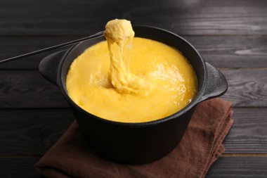 Jambonu fondü kabına daldırmak, erimiş peyniri siyah ahşap masaya koymak, yakın plan.