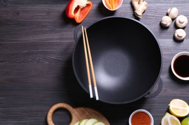 Boş demir tava, yemek çubukları ve malzemeler koyu gri ahşap masa, düz yatak. Metin için boşluk