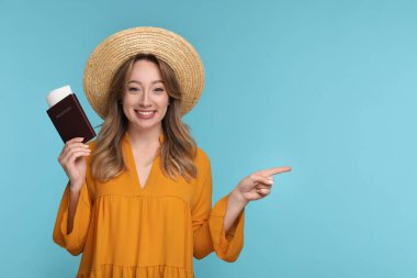 Pasaportu, bileti ve şapkası olan mutlu genç bir kadın açık mavi arka planda bir şeyi işaret ediyor. Mesaj için yer var.