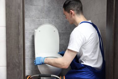 Su dolabında klozet tamir ederken koruyucu eldiven giyen genç bir tesisatçı.