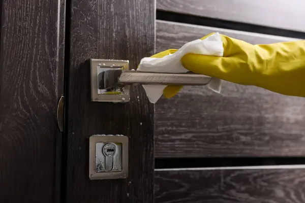 Woman cleaning door handle with detergent and paper towel, closeup