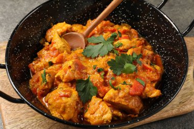 Gri masada tavada ve kaşıkta leziz körili tavuk, yakın plan.