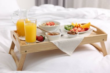 Yatakta servis edilen lezzetli kahvaltı. Yulaf ezmesi, meyve suyu, meyve, badem ve bal ahşap tepside.