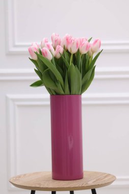 Beyaz duvarın yanındaki masada taze pembe laleler.