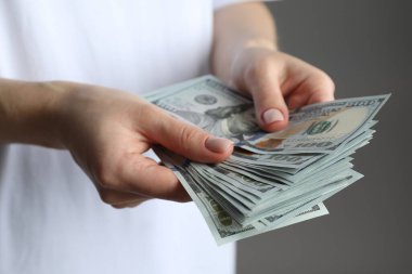 Para değişimi. Gri arka planda dolar banknotları sayan kadın, yakın plan.