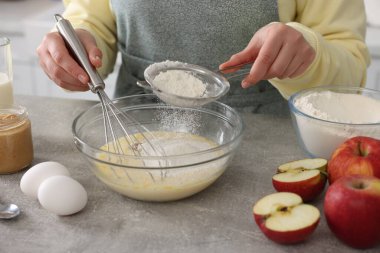Kapalı mekandaki gri masada un ellerken yumurta çırpan kadın, yakın plan.