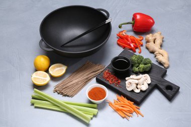 Wok, yemek çubukları ve gri masadaki farklı ürünler.