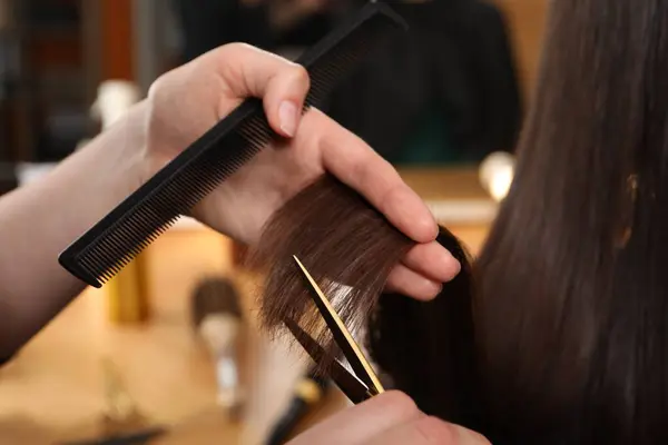 Hairdresser cutting client\'s hair with scissors in salon, closeup