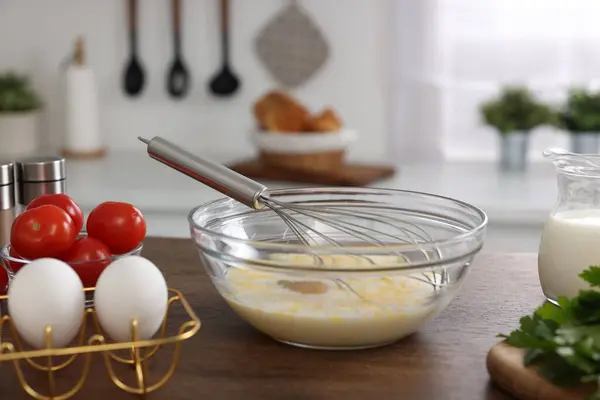 Whisk, bowl, beaten eggs and other ingredients on wooden table indoors
