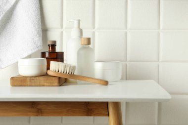 Duvarın yanındaki beyaz masada farklı banyo aksesuarları ve kişisel bakım ürünleri var.