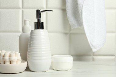 Duvarın yanındaki beyaz masada farklı banyo aksesuarları ve kişisel bakım ürünleri var.