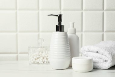 Duvarın yanındaki beyaz masada farklı banyo aksesuarları ve kişisel bakım ürünleri var.