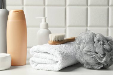 Duvar kenarındaki beyaz masada banyo aksesuarları ve kişisel bakım ürünleri, yakın plan.