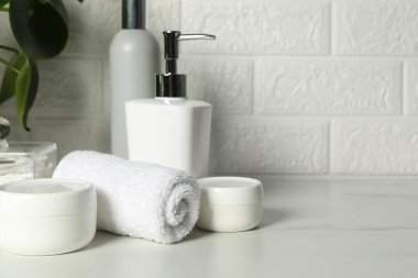 Farklı banyo aksesuarları ve kişisel bakım ürünleri tuğla duvarın yanındaki beyaz masada, metin için yer var.